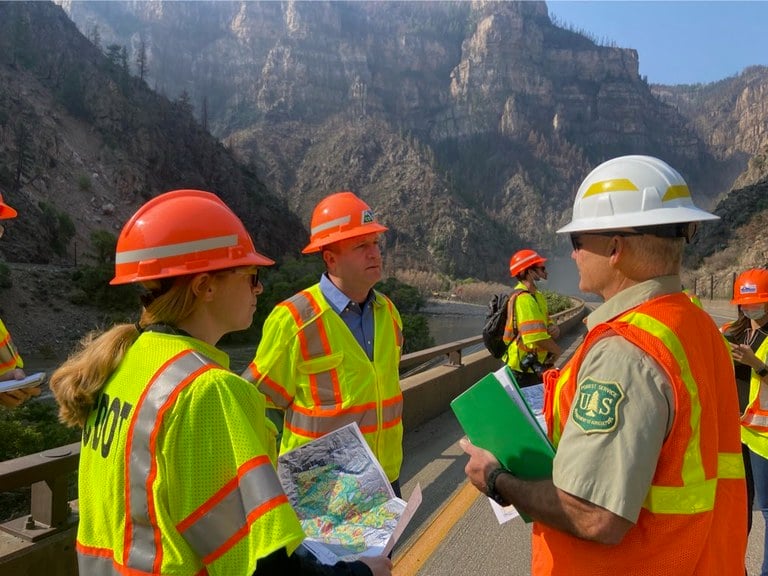 Governor Polis, CDOT Director Lew, State Officials and members of the media observe the damage and repairs
