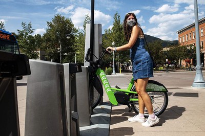 Woman parking electric bicycle at bike sharing rack. 
