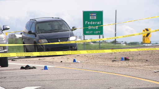 A van pulled over on the side of the road next to a road sign that says, "Federal Blvd next left." Debris litters the road and caution tape surrounds the area.